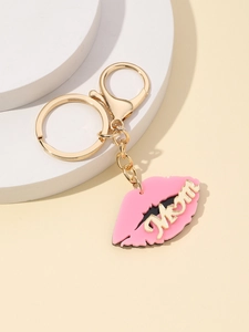 Detail of pink lip keychain with gold MOM lettering and chain on a minimalist pedestal