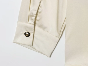 Détail du poignet d'un chemisier en satin de soie crème avec bouton en métal doré