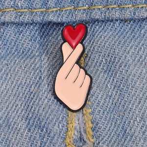 Macro shot of cute cartoon hand heart alloy enamel pin on blue denim jacket texture