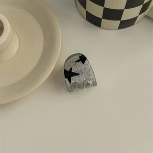 Detail view of a mini silver hair claw with black stars on a checkerboard background