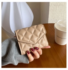 Close-up of a hand holding a khaki quilted leather mini wallet in a soft lifestyle setting