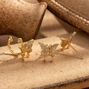 Sparkling gold butterfly earrings set with zircon stones on a warm textured surface