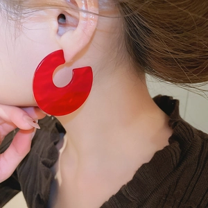 Detail of red marble acrylic C-shaped earrings worn by a model in warm lighting
