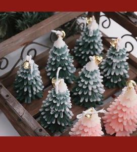 Top view of green and pink snow-covered Christmas tree candles with gold bells in a crate