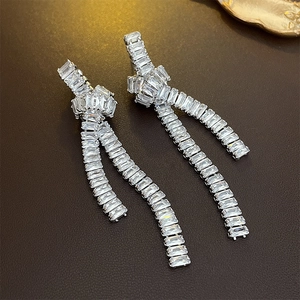 Close-up of silver tassel earrings with emerald-cut cubic zirconia and knot detail