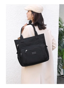 Détail d'un grand sac cabas noir en nylon avec poches zippées porté par un mannequin en extérieur