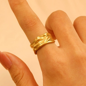 Detailed close-up of wide golden stainless steel ring with irregular wavy texture on finger