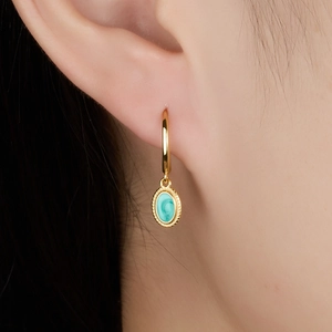 Detailed shot of a gold turquoise hoop earring with beaded edge on model's ear