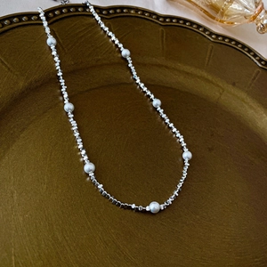 Detail view of irregular silver beads and pearls on a vintage bronze display tray