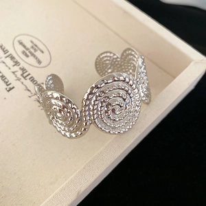 Detailed macro view of silver open cuff bracelet with spiral swirl texture and metal discs