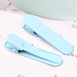 Macro detail of two light blue seamless metal duckbill hair clips on white cardstock
