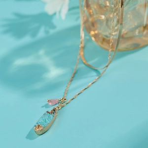 Double-layer gold necklace with blue druzy and pink teardrop pendant on blue background