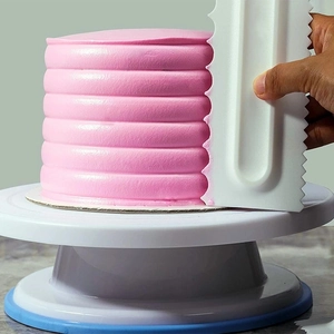 Detail showing a white plastic cake scraper creating textured patterns on pink frosting