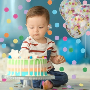 Toddler celebrating with birthday cake surrounded by colorful confetti and gold sequins balloons