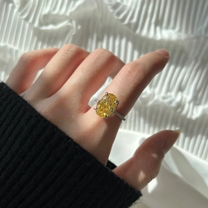 Detailed view of an oval yellow zircon ring with silver halo setting worn on a hand