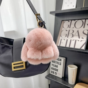Pink plush rabbit keychain with gold ring on black bag in a stylish lifestyle setting