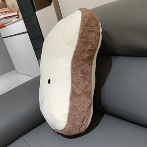 Close-up of a soft toast bread plush pillow with an embroidered smiley face on a sofa