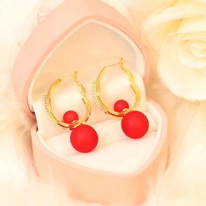 Close-up of gold hoop earrings with red matte beads in a heart-shaped jewelry box