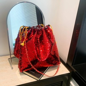 Detail of red sequin bucket bag with yellow drawstring and gold chain strap on marble