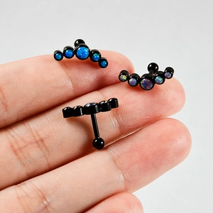 Macro shot of curved black steel cartilage studs with five opal stones on fingertip