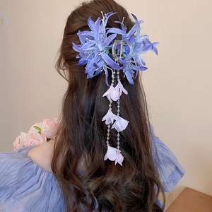 Détail d'une pince à cheveux fleurie avec pétales en tissu bleu et longs glands