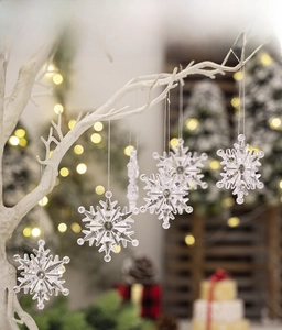 Detail of clear acrylic snowflake ornaments hanging on a white branch with bokeh lights