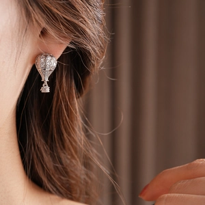 Détail de boucles d'oreilles montgolfière en zircone portées par un mannequin sur tissu