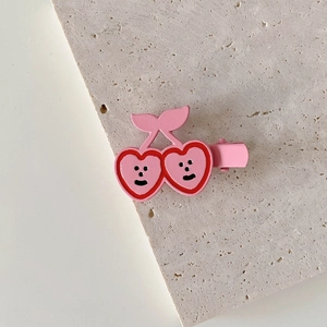 Detailed view of a cute pink cherry hair clip with a smiling face and metal duckbill base