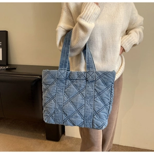 Détail d'un sac cabas en jean matelassé bleu porté par un mannequin dans un cadre épuré
