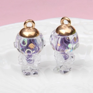 Detail of two transparent astronaut glass pendants with purple glitter on a white plate
