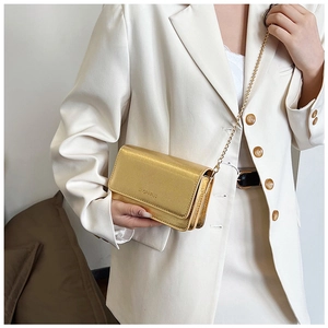 Detail of a shiny gold chain bag with embossed texture worn with a white blazer