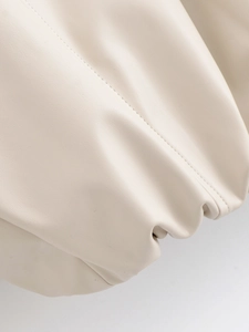 Detailed close-up of beige faux leather texture and fine stitching on a lapel jacket