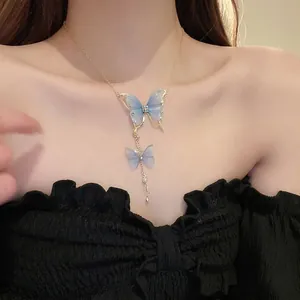 Golden necklace with blue tulle butterfly pendants and pearls worn on a model's neck