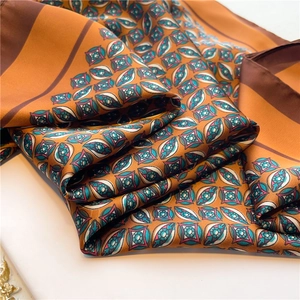 Close-up of luxury satin square scarf featuring geometric patterns in orange and blue