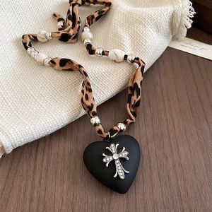 Detailed macro view of matte black heart pendant with sparkling rhinestone cross and leopard cord