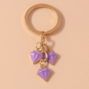 Detail of golden keychain with three purple diamond-shaped enamel pendants on warm background