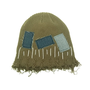 Detailansicht der Distressed-Jeans-Patches und Fransen am olivgrünen Strickbeanie