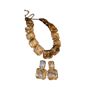 Set collana e orecchini con strass quadrati dorati e pietre preziose su sfondo bianco
