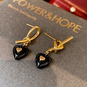 Macro view of gold-plated knot earrings with black heart charms and engraved display card