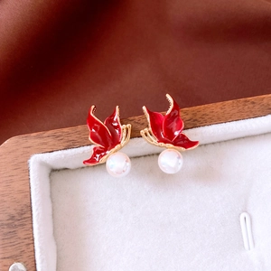 Détail de boucles d'oreilles papillon dorées avec émail rouge et perles en écrin blanc