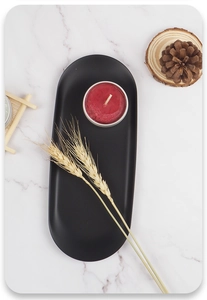 Flat lay of a matte black oval metal tray with a red candle on marble surface