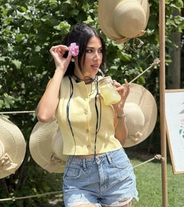 Detail of a casual sleeveless yellow linen vest paired with denim shorts in a summer setting