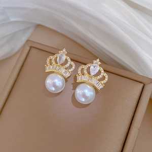 Close-up of golden crown pearl earrings with sparkling white zircons on leather