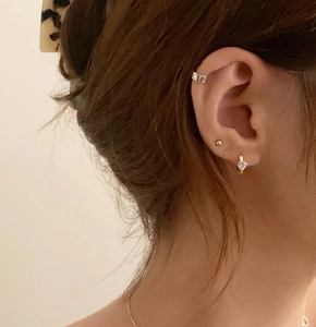 Close-up of heart cubic zirconia stud, gold bead earring, and silver ear cuff on ear