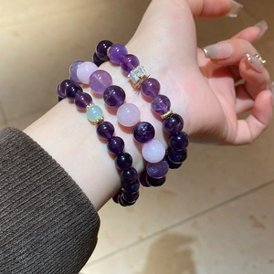 Detailed view of layered amethyst and quartz beaded bracelets with gold diamond charms