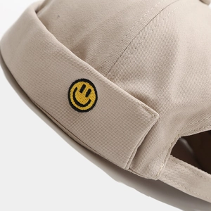 Close-up of yellow smiley face embroidery and twill cotton texture on a beige docker hat