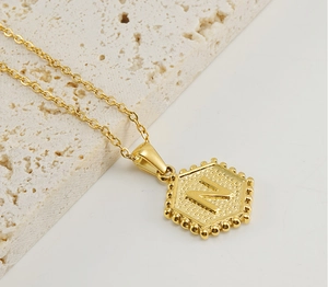 Detail of golden hexagon N letter pendant with beaded edges on a minimalist O-chain necklace