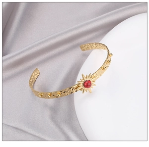 Detailed close-up of a gold hammered C-shape bangle with a red stone in starburst setting