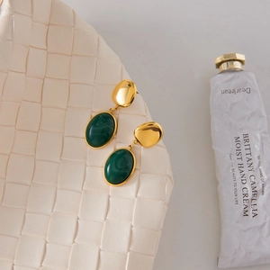 Elegant gold titanium steel earrings with green resin pendants on white woven background