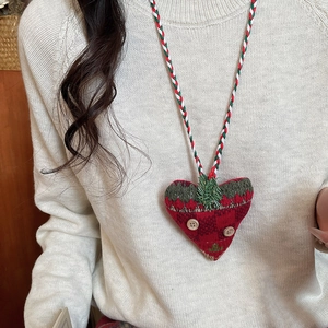 Detail view of a red heart plush pendant on a colorful knitted rope Christmas necklace